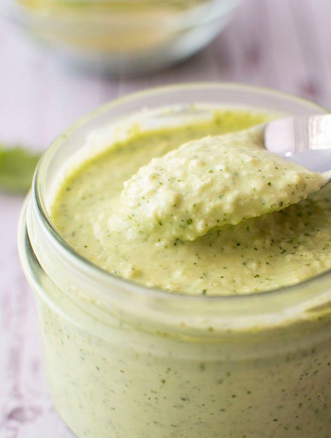 A spoonful of avocado, jalapeno and lime crema being lifted out of a small jar.