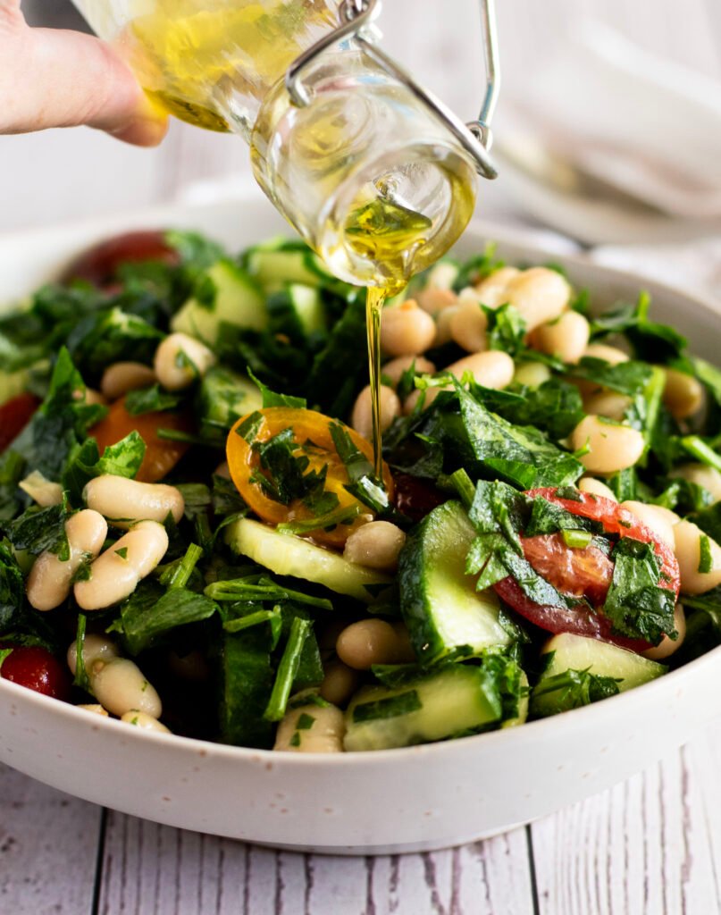 Hand drizzling the zesty lemon dressing over the cannellini bean salad.