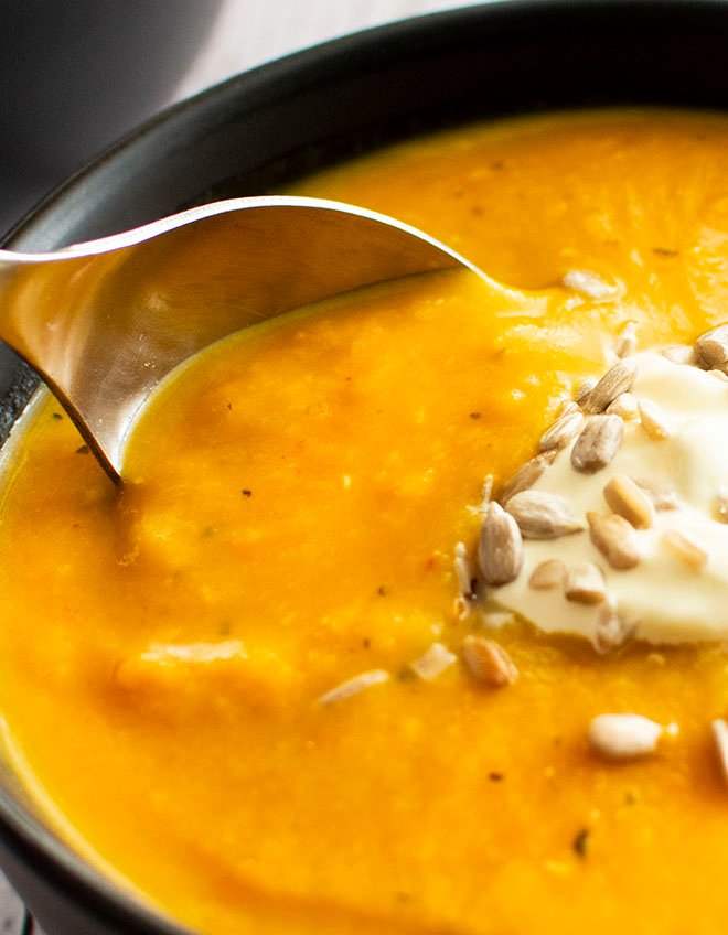A spoon being dipped into a bowl of pumpkin, sundried tomato and lentil soup.