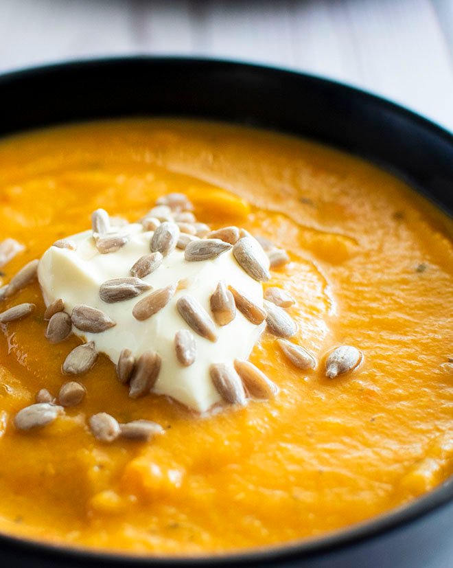 A bowl of pumpkin, sundried tomato and lentil soup topped with a dollop of greek yoghurt and sunflower seeds.