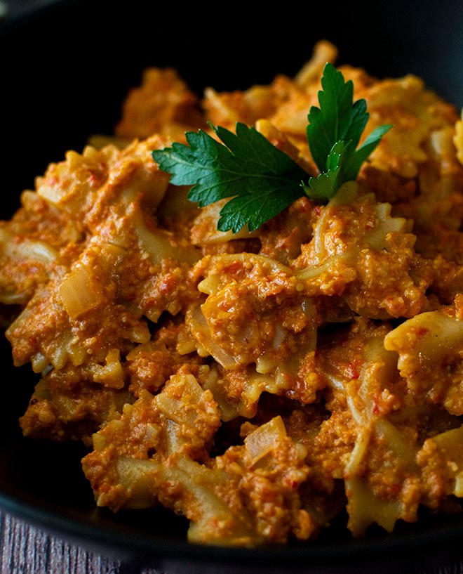 A close up of a bowl of roast pepper and cashew pesto pasta.