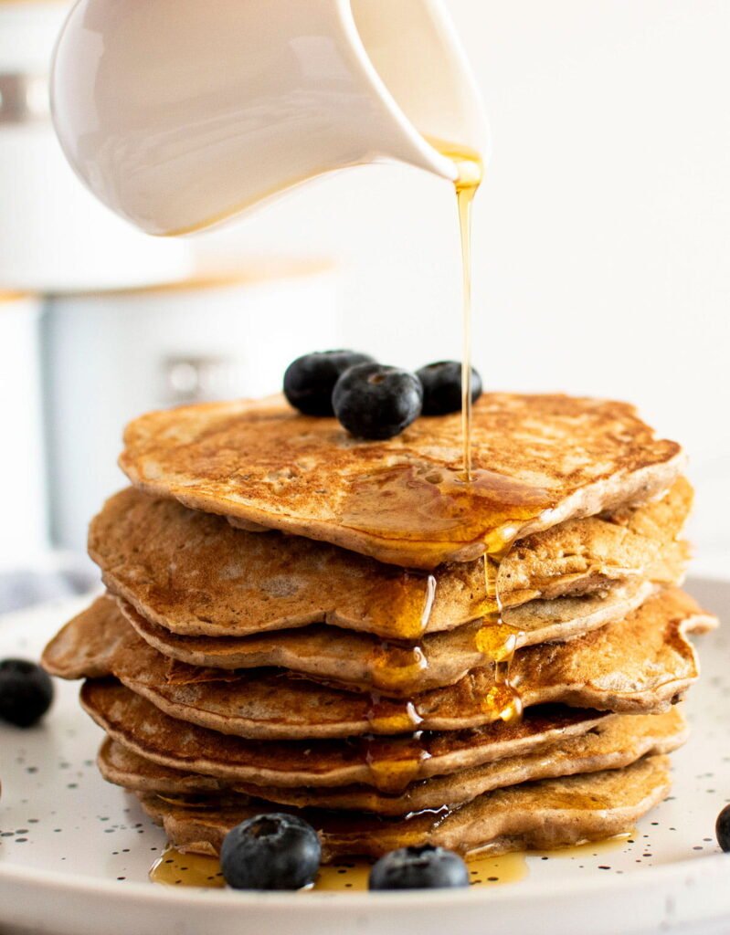 A jug pouring maple syrup on banana buckwheat pancakes,