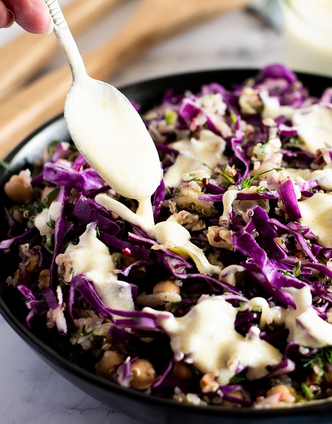 Creamy greek yoghurt dressing being drizzled onto a bowl of dill, apple and red cabbage slaw.