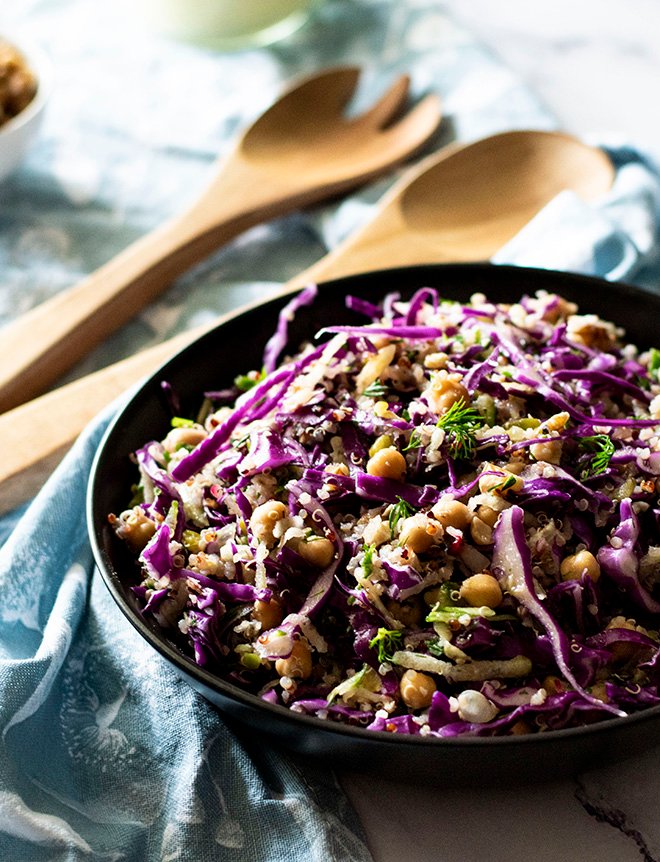 A bowl of dill, apple and red cabbage slaw with wooden salad spoons in the background.