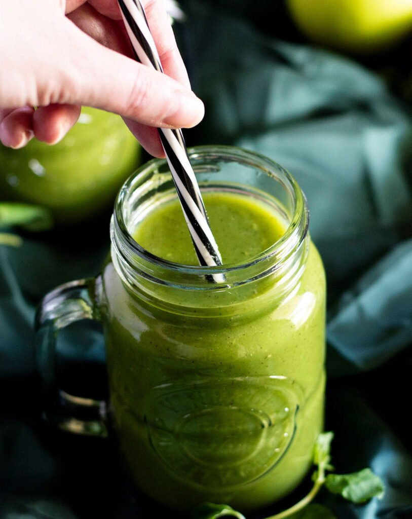 A hand placing a straw in a mason jar filled with fresh kiwi juice.