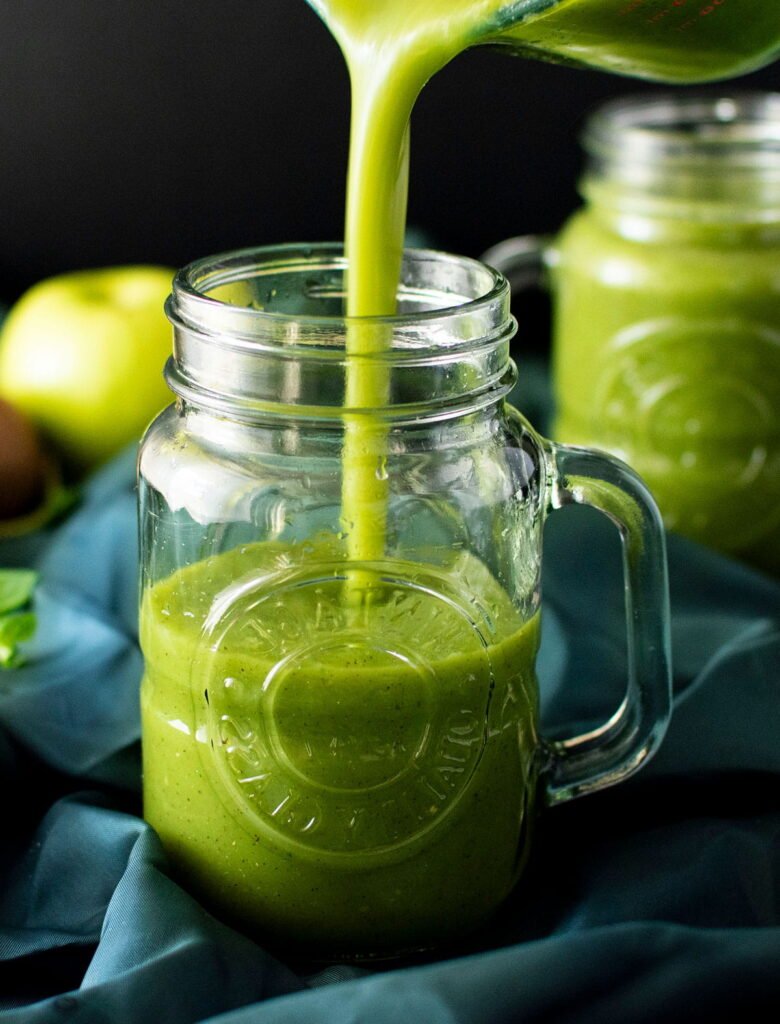 Fresh kiwi juice being poured into a mason jar with a handle.