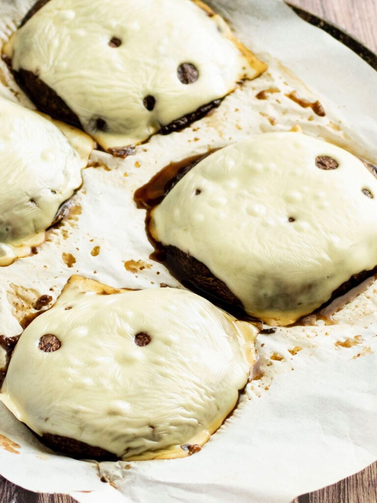 A tray of oven baked portobello mushroom burgers with swiss cheese on top.