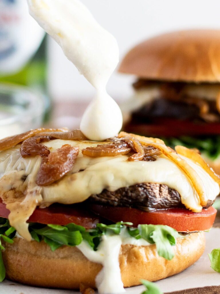 A dollop of yoghurt truffle sauce being drizzled onto a portobello mushroom burger.