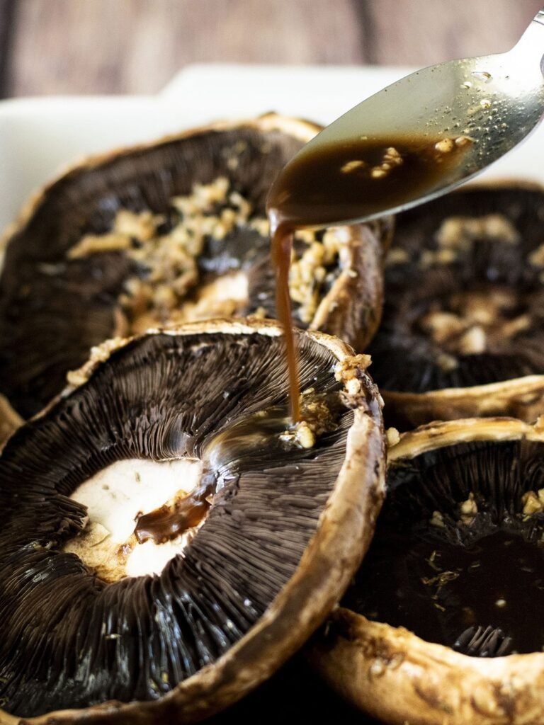 Balsamic marinade being drizzled onto portobello mushrooms.