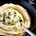 A bowl of potato and white bean mash with a spoon.