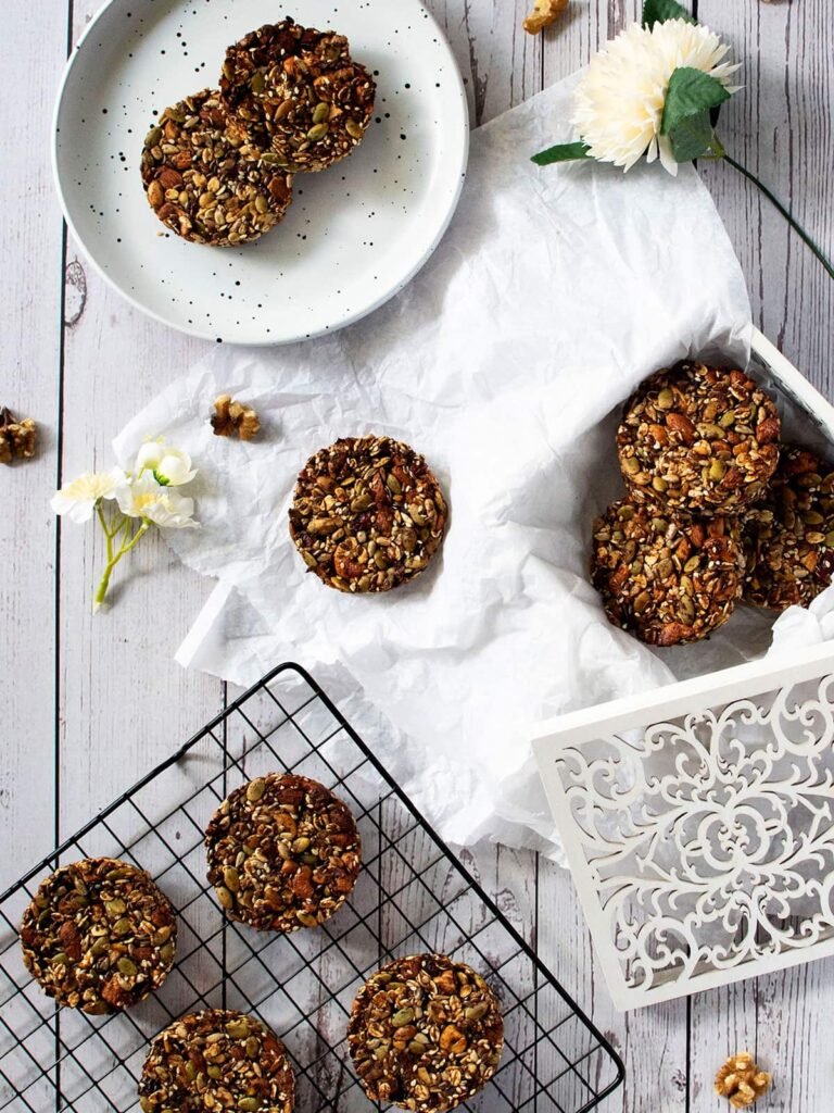 Cranberry and mixed nut cookies on a side plate, cooling rack and inside a white ornate box with crumpled paper.