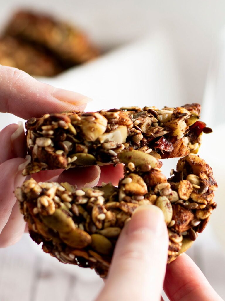 Two hands breaking apart a cranberry and mixed nut cookie.