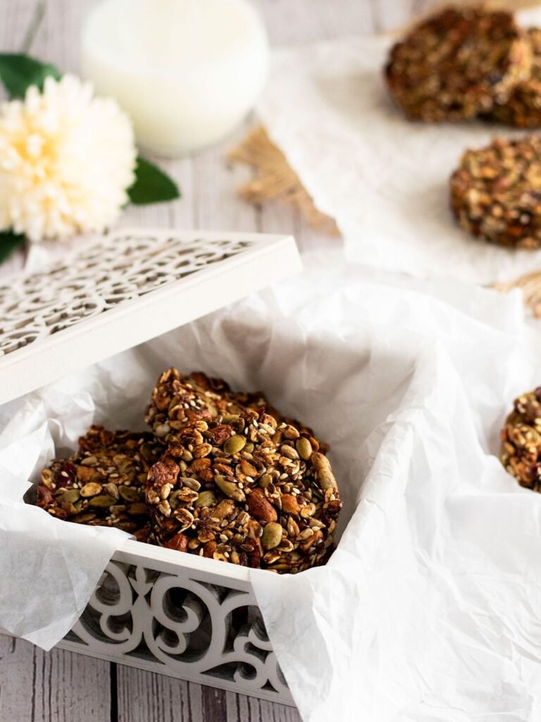 A white ornate box filled with cranberry and mixed cookies and crumpled white paper hanging over the sides.