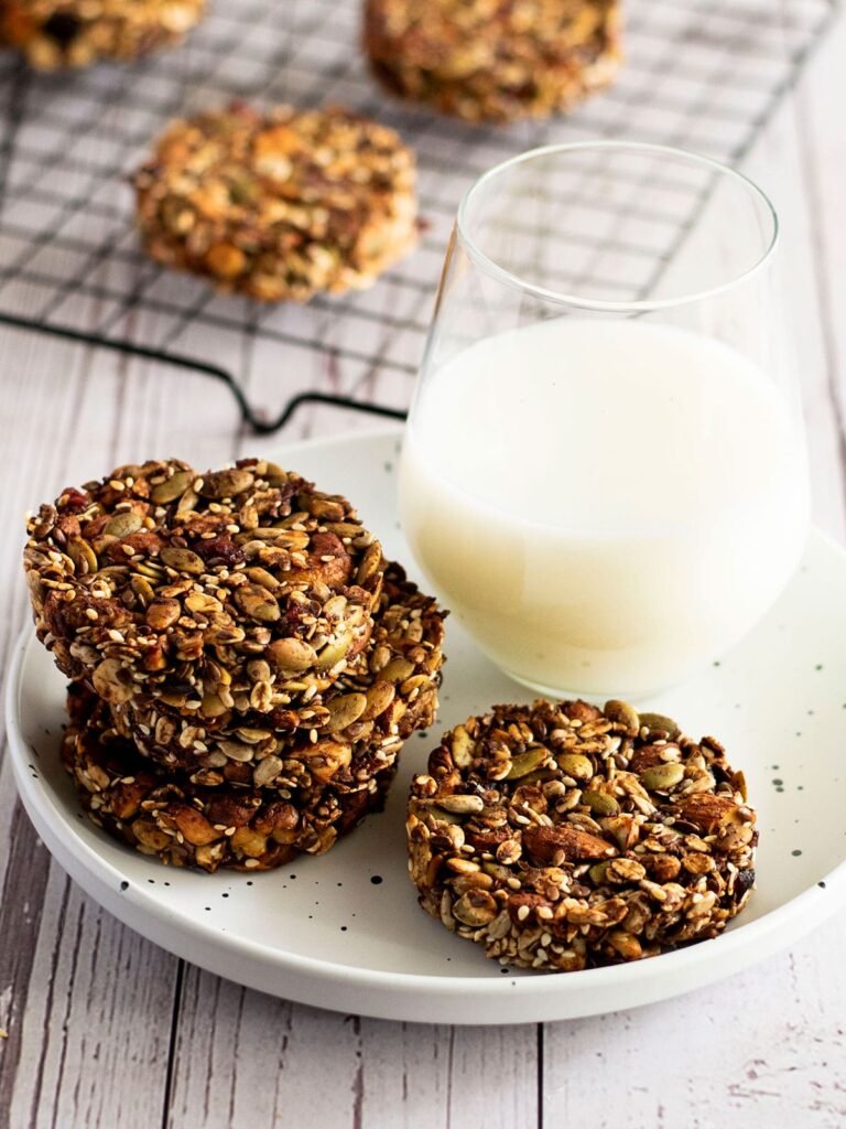 Four mixed nut cookies on a side plate with a glass of milk.