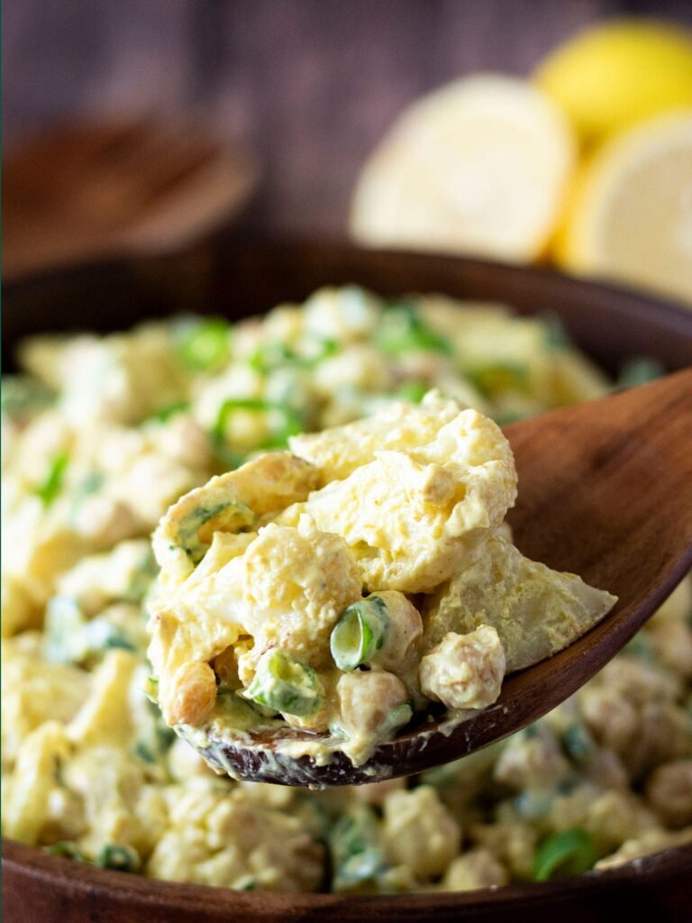 A wooden spoon lifting a spoonful of curry cauliflower potato salad out of a bowl.