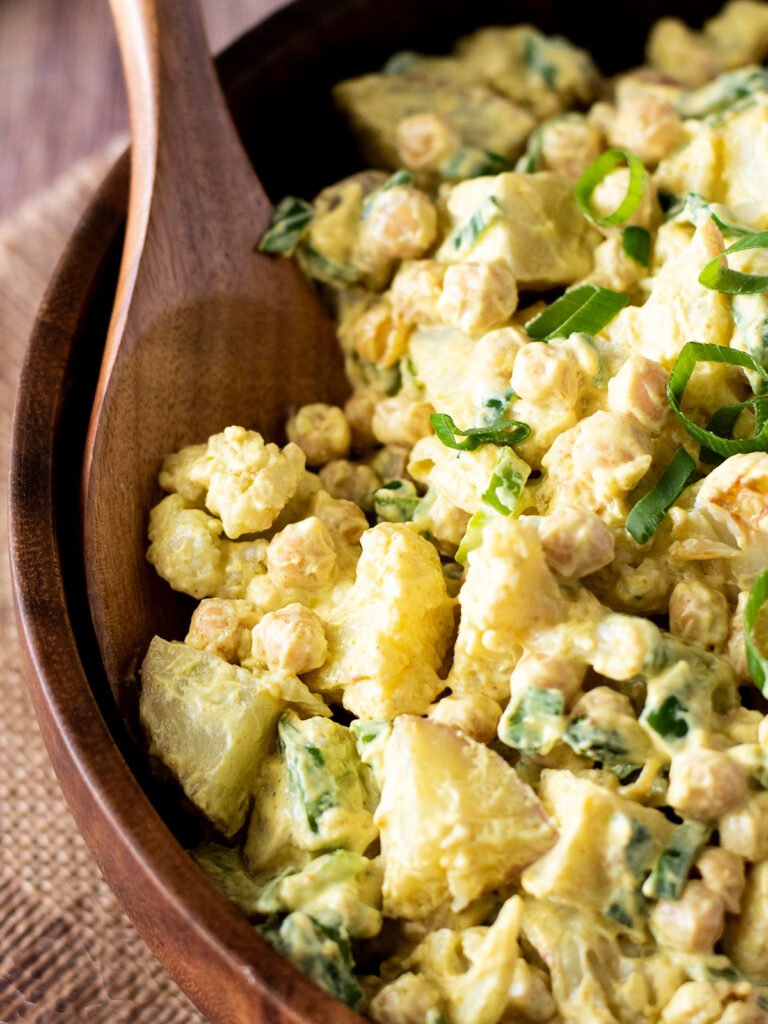 A wooden spoon in a bowl with curry cauliflower potato salad.