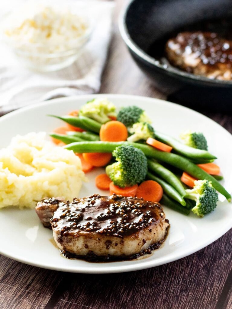 A pan fried pork steak with balsamic glaze on a dinner plate with vegetables.