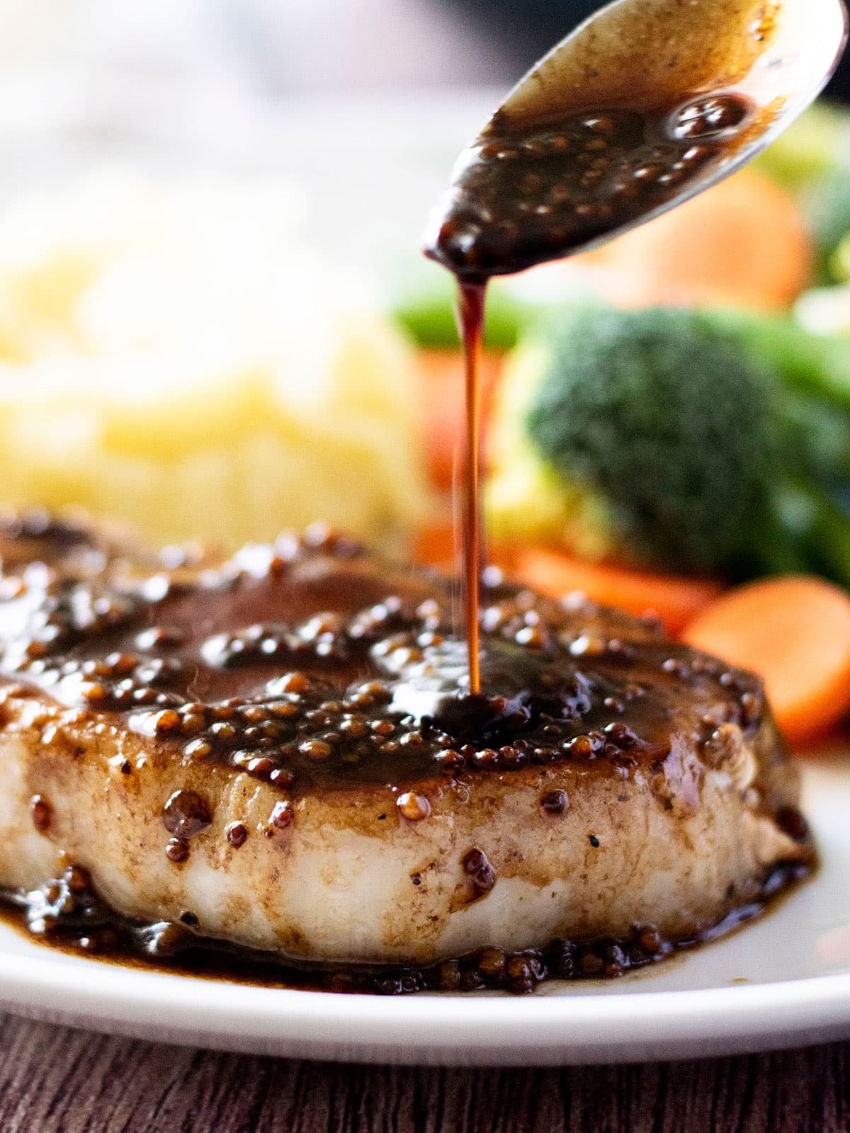 A spoon drizzling balsamic reduction over a pan fried pork steak.