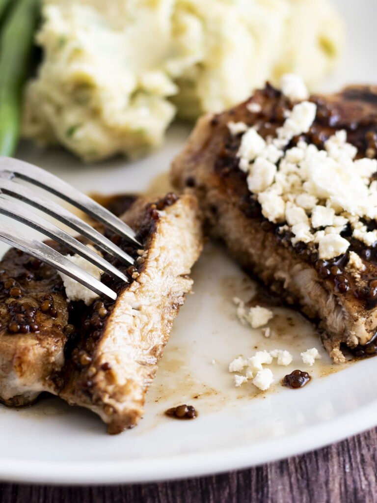 A pan fried pork steak with balmsaic glaze and fetta cheese cut in half.