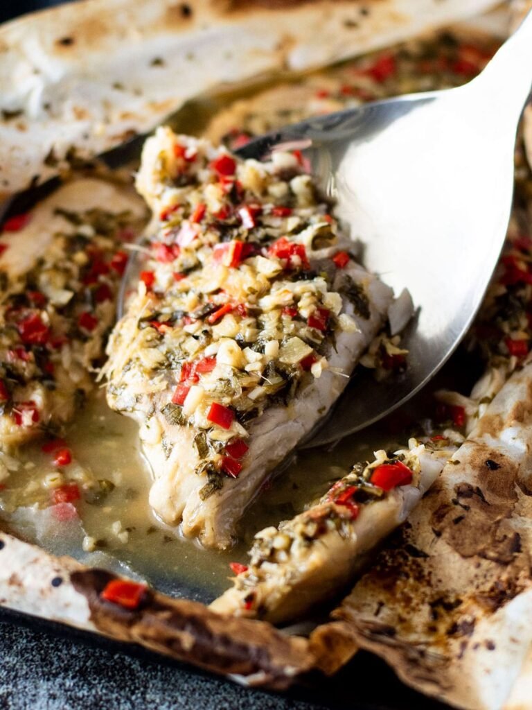 A lable scooping out a piece of baked barramundi with thai sauce.