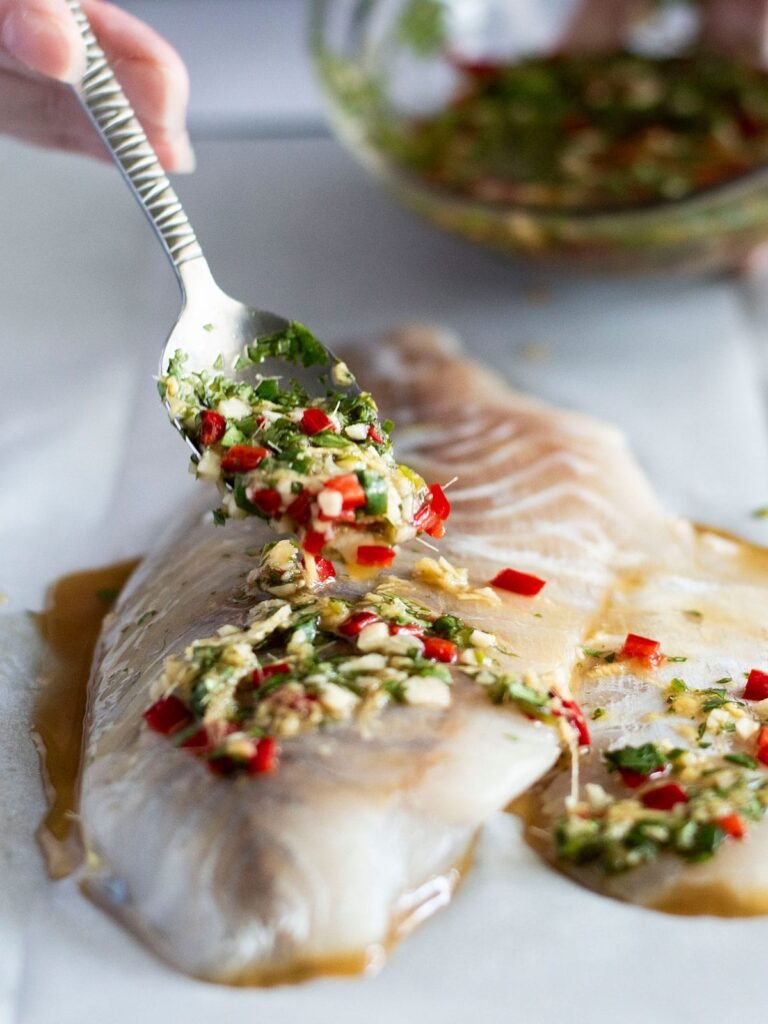 Thai sauce being spooned onto a piece of fish for baked barramundi.