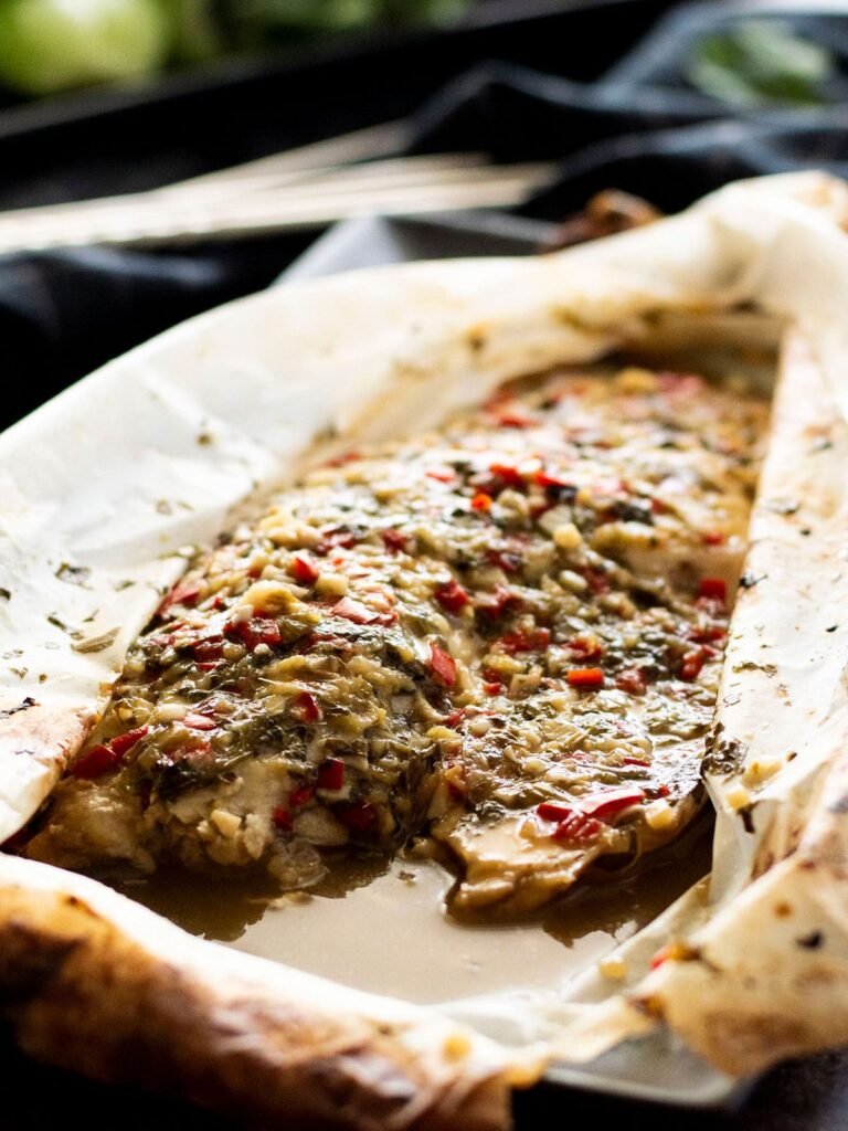 A piece of baked barramundi with Thai sauce in parchment paper.