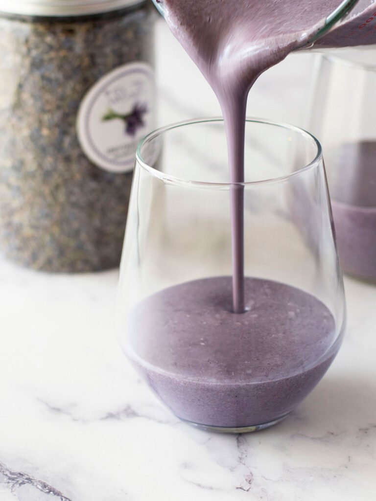 A jug pouring lavender and blueberry panna cotta mix into a glass.