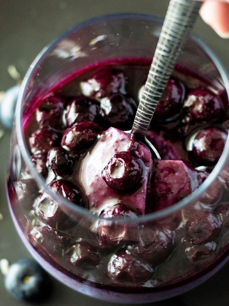 A spoon scooping out a piece of lavender and blueberry panna cotta with blueberry sauce.