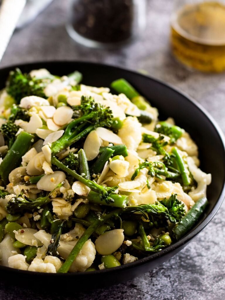 A bowl of warm broccolini salad with feta and almonds.