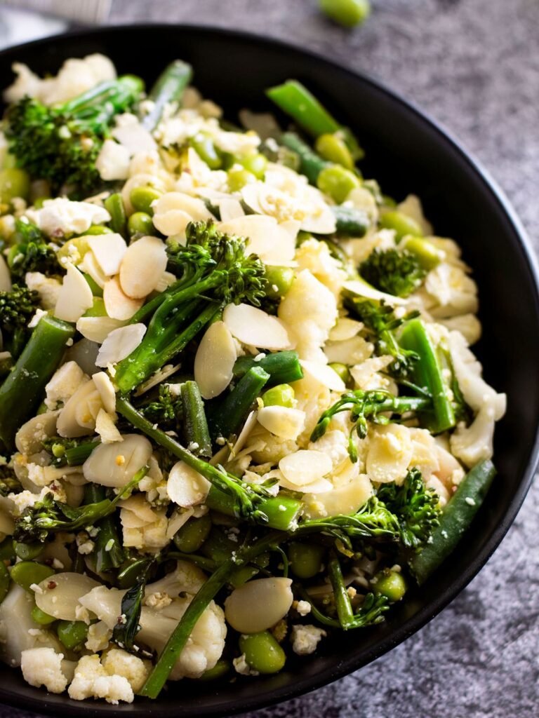 A bowl of warm broccolini salad with feta and almonds.