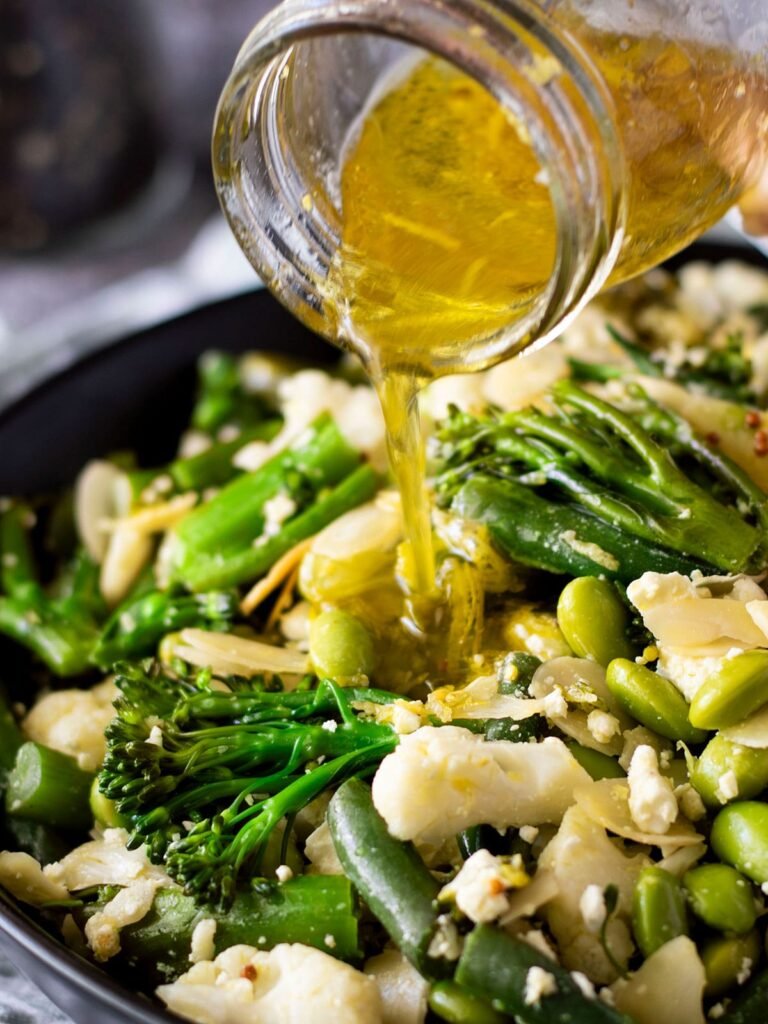 Dressing being drizzled onto warm broccolini salad.