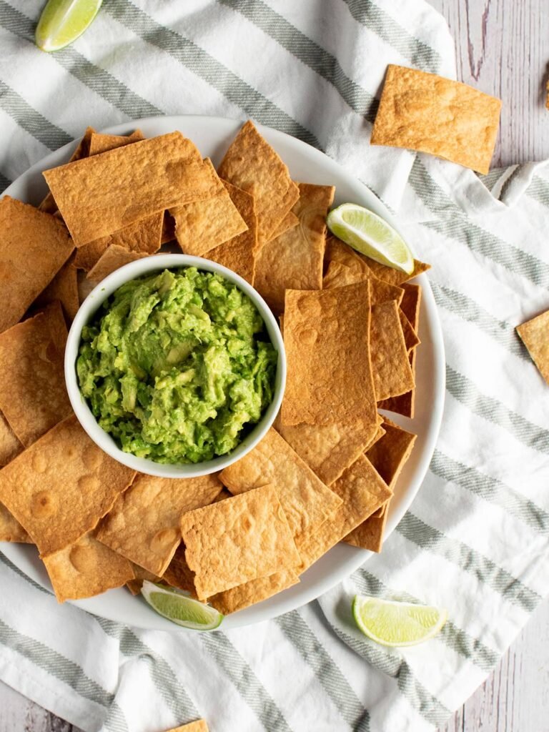 A plate full of tortilla chips around a bowl of guacamole.