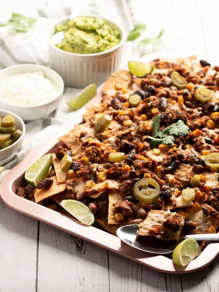 A sheet pan full of beef and bean nachos with sides.