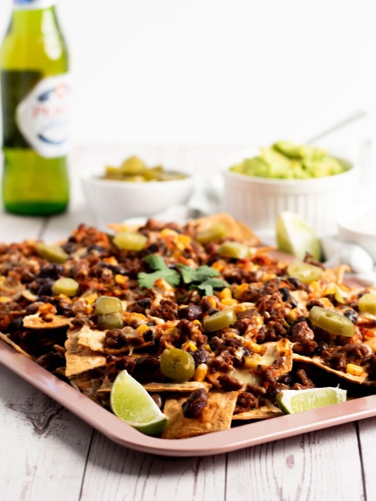 A tray of beef and bean nachos with a beer and sides in the background.