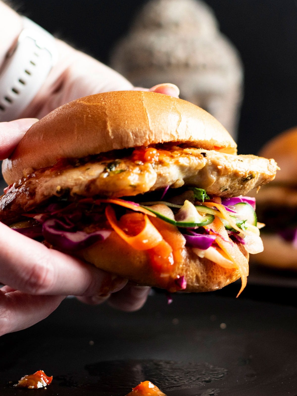 Hands holding a juicy Thai Chicken Burger.