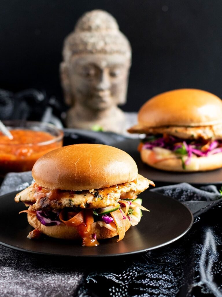 Two thai chicken burgers on black plates.