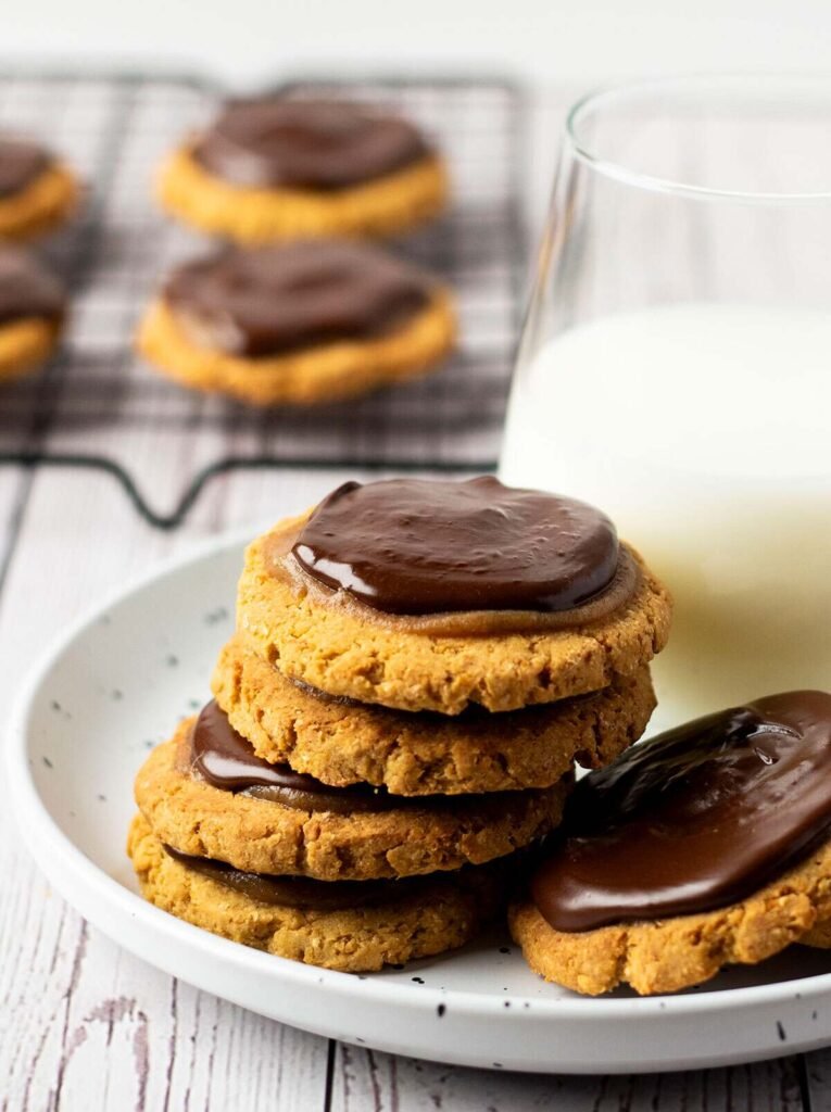 Twix cookies stacked on a plate with a glass of milk.