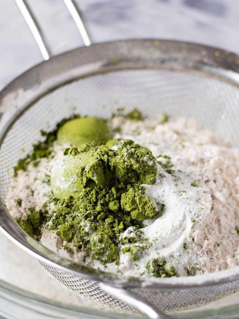 A sieve full of dry ingredients for pistachio and matcha cake.