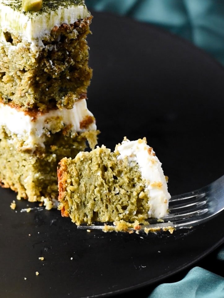 A fork holding a piece of pistachio and matcha cake.