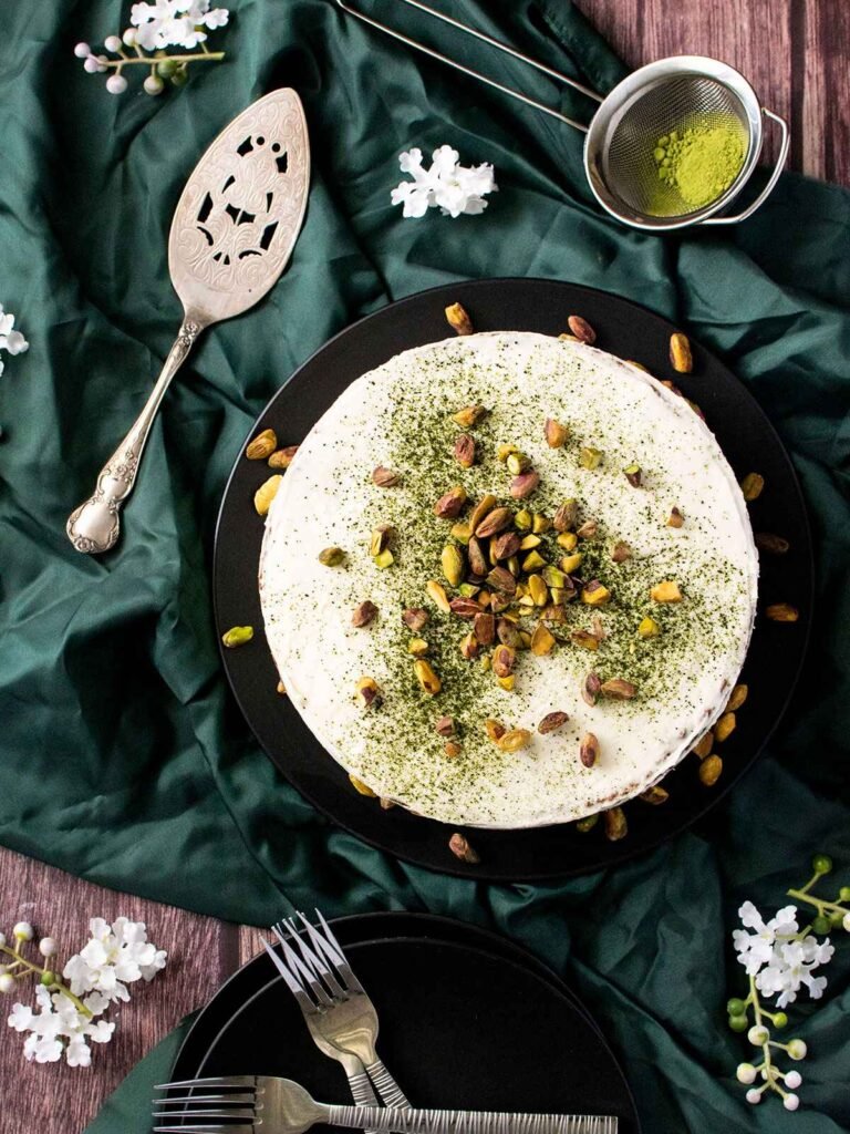 A pistachio and matcha cake on a black plate on top of ruffled green satin.