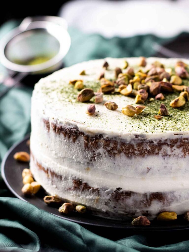 A pistachio and matcha cake on a black plate on top of ruffled green satin.