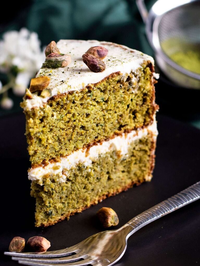 A piece of pistachio and matcha cake on a black plate.