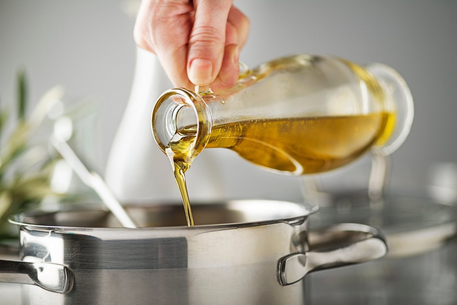 A hand pouring extra virgin olive oil into a cooking pot.