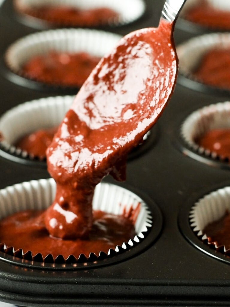 A spoon dripping chocolate beetroot cupcake batter into a liner.