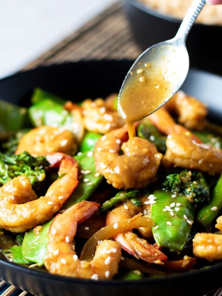 A spoon dripping sauce onto a bowl of Chinese curry prawns.