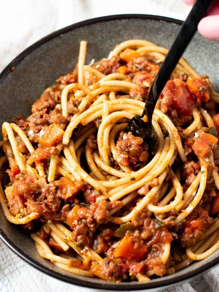 A fork twirling pasta coated in beef and lentil bolognese sauce.